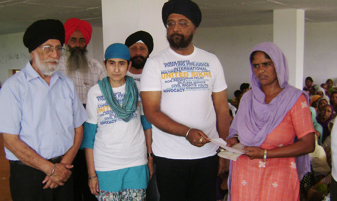 Pinderpal Singh hands over a cheque to a woman in Gurney Kalan village in Sangrur district