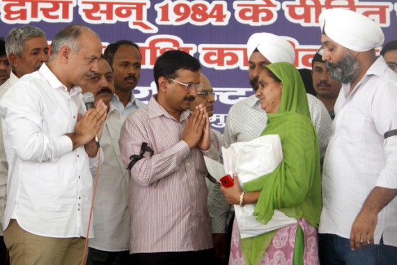 Delhi Chief Minister Arvind Kejriwal (C) hands over relief cheques to the families of the 1984 Sikh genocide victims as Deputy CM Manish Sisodia
