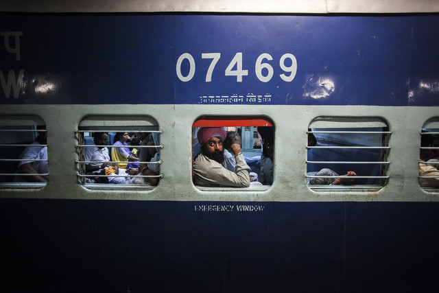 A passenger looks out of a carriage window as the passenger opposite him lies on his seat on the Abohar-Jodhpur passenger train also known by the locals as the Cancer Express in Bhatinda, Punjab. [Prashanth Vishwanathan (Bloomberg)]